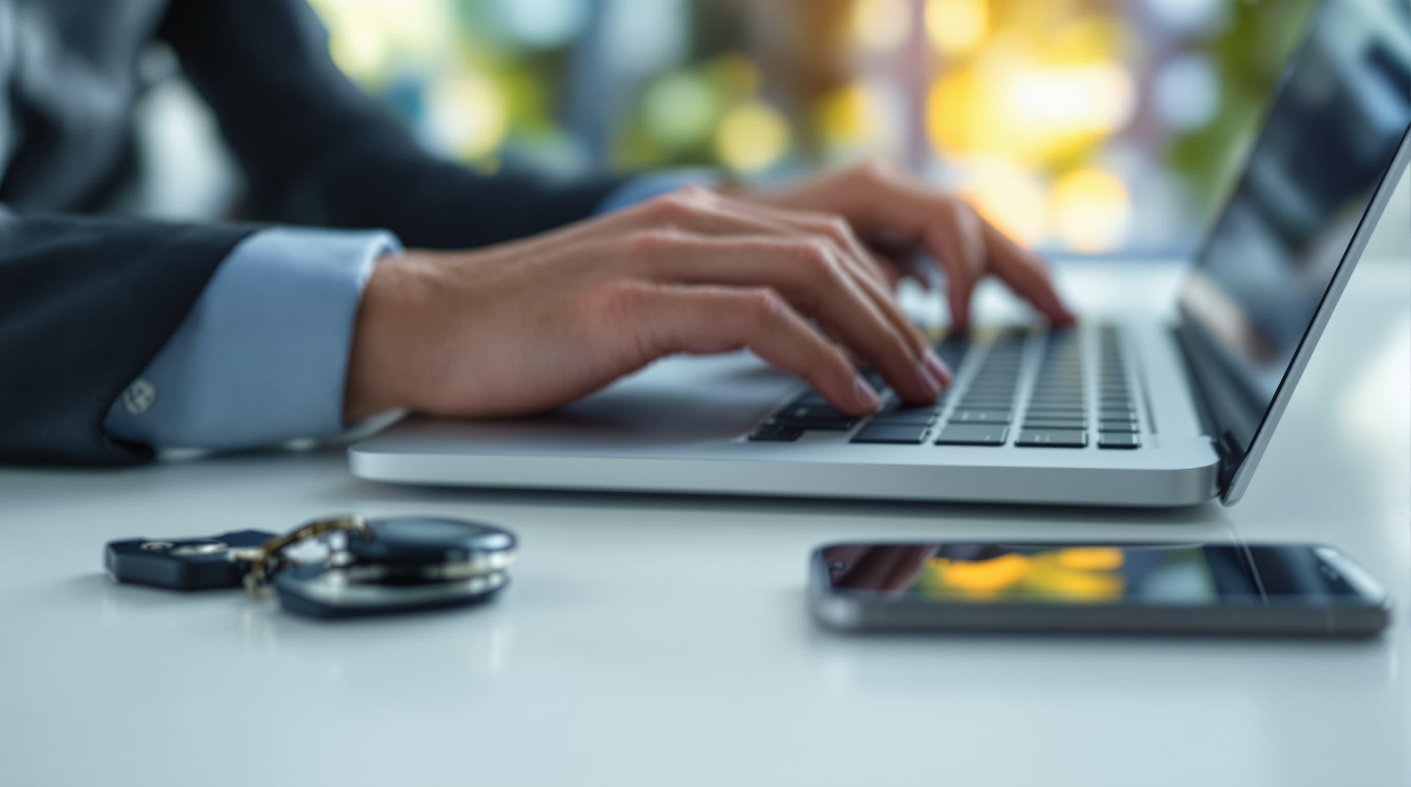 Hände auf einer Laptop-Tastatur, daneben ein Schlüsselbund und ein Smartphone